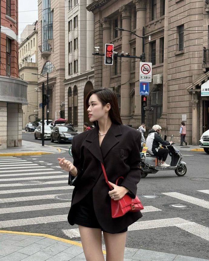 Đỗ Thị Hà diện blazer và quần short, điểm nhấn là túi xách đỏ.