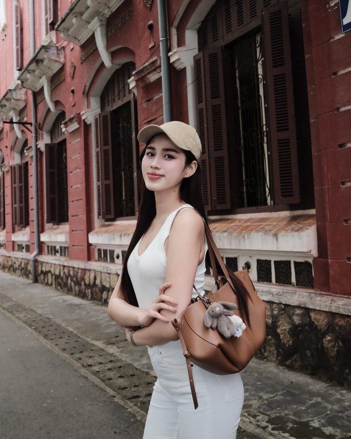 Đỗ Thị Hà diện áo tank top và quần jeans trắng, kết hợp mũ lưỡi trai và túi xách nâu.